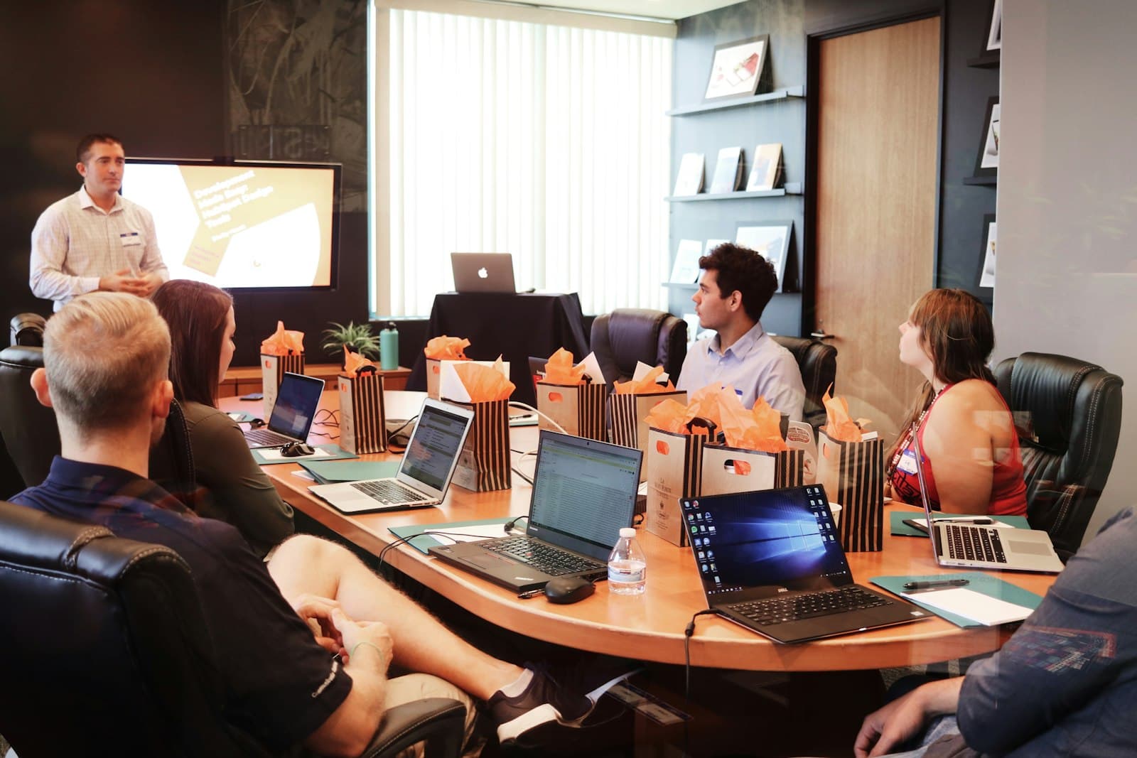 A team meeting around a table with laptops and a presenter
